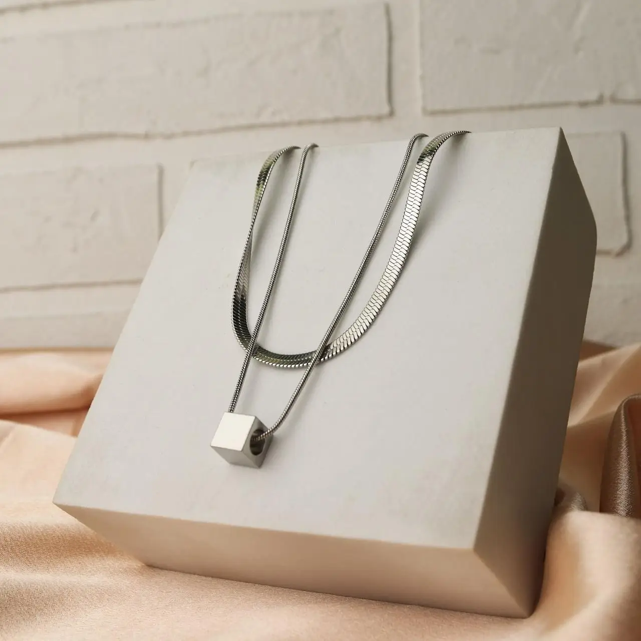 Two layered steel chains with a small cube pendant on a display block