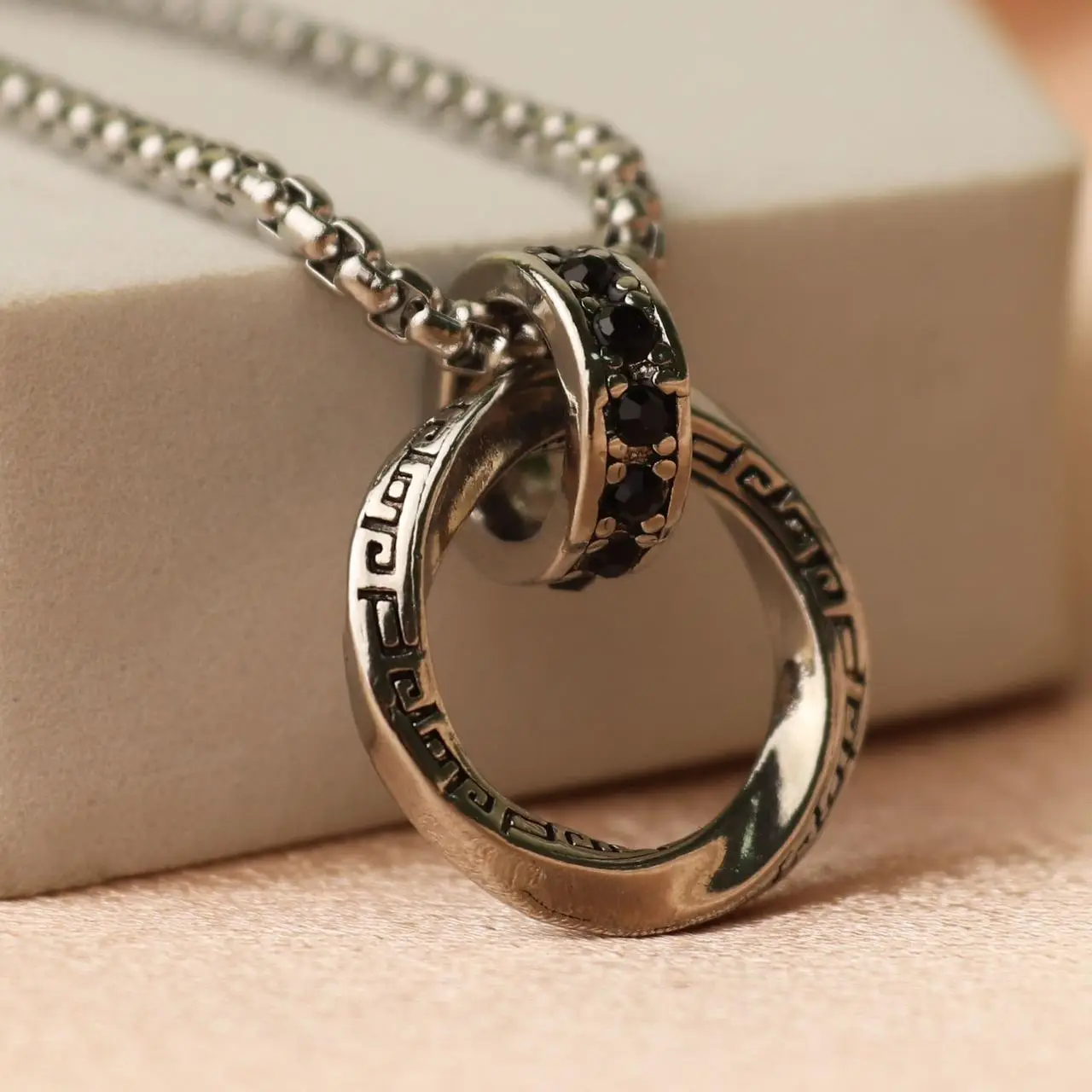 Two interlocking rings pendant, one engraved with a meander pattern, one set with black stones