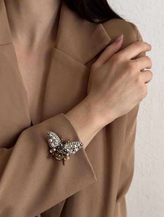 Beaded moth brooch with pearls pinned to a camel coat sleeve